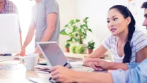 Two young colleagues seated and collaborating in the foreground and two colleagues standing and collaborating in the background