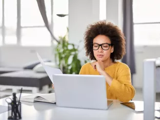 Woman working at home office with laptop and printed documents