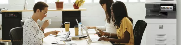 Three workers at communal desk with a printer in the background